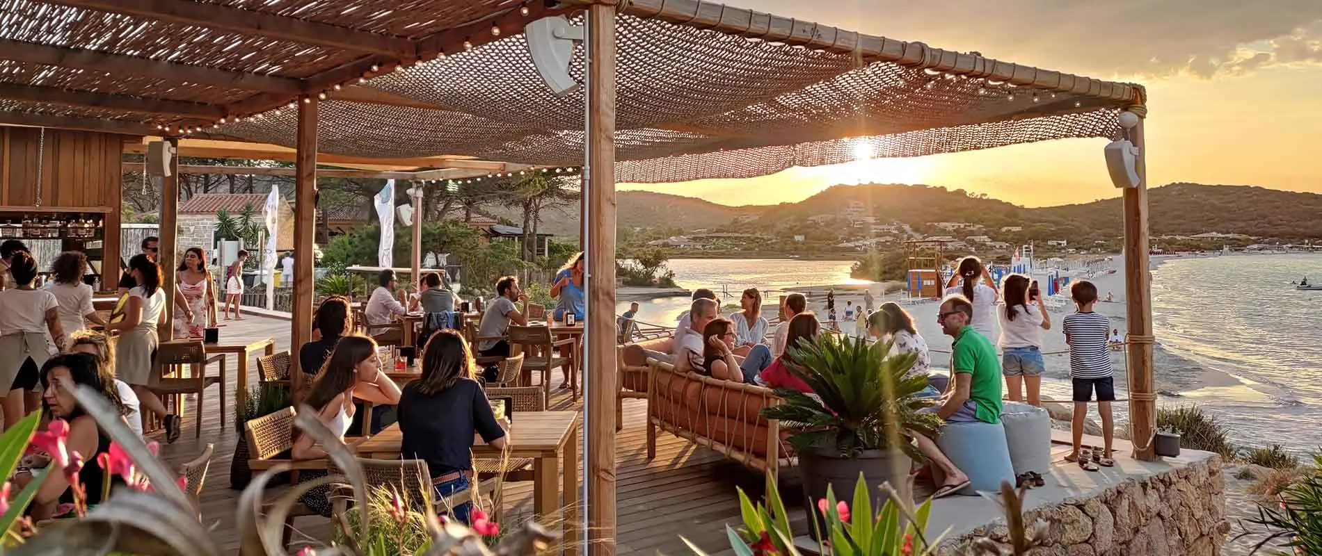Sunset over Porto Taverna seen from the Tavernetta beach bar terrace, guests gathered under the pergola