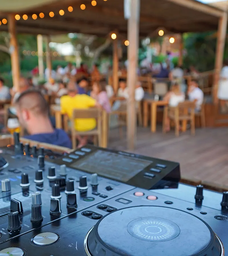 DJ console at the beach bar with the evening crowd under string lights behind