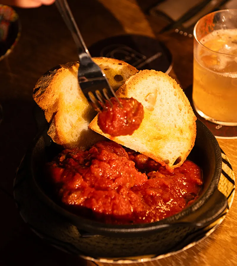 Cast-iron dish of meatballs in tomato sauce with toasted bread and a cocktail at Jaga