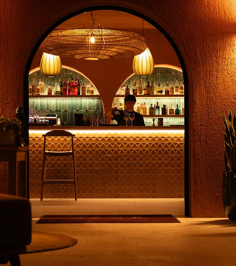 Arched entrance of the Jaga cocktail bar at night, bartender at work behind the warmly lit counter