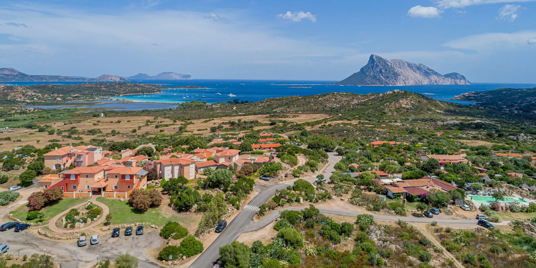 Aerial view of the terracotta roofs of Lu Nibareddu on the Monte Petrosu hill, Tavolara behind