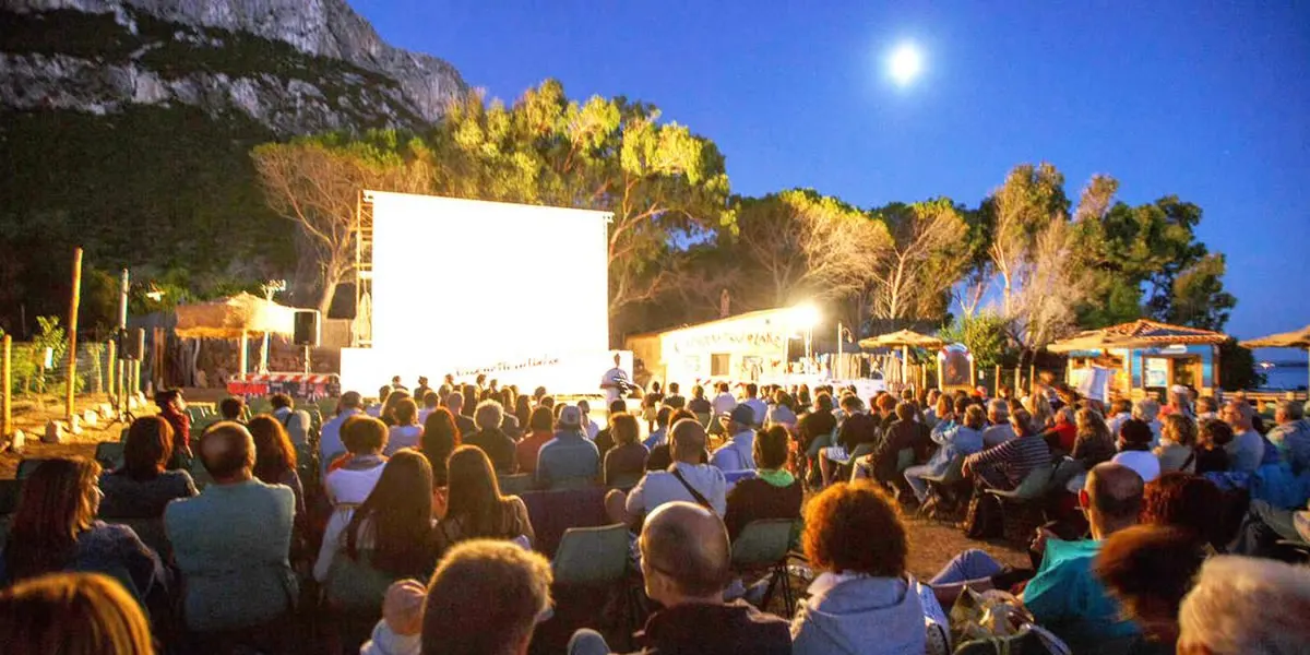 Open-air cinema audience at dusk beneath the cliffs of Tavolara
