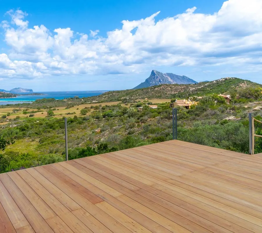 Empty wooden yoga deck above the Mediterranean macchia, looking out over the bay to Tavolara island