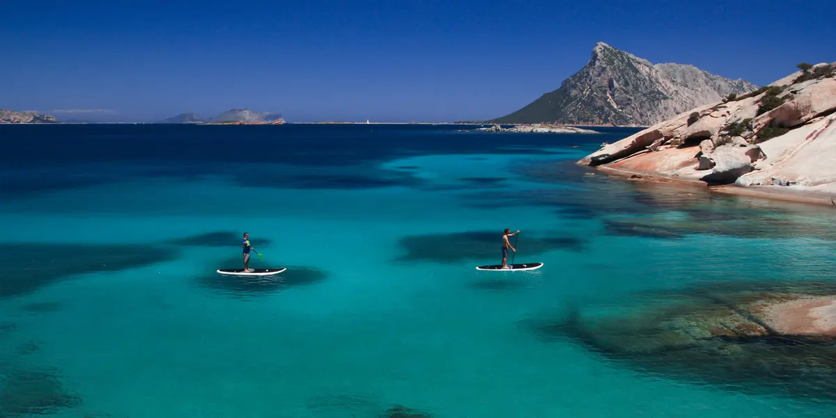 Two paddleboarders crossing the turquoise bay toward Tavolara island