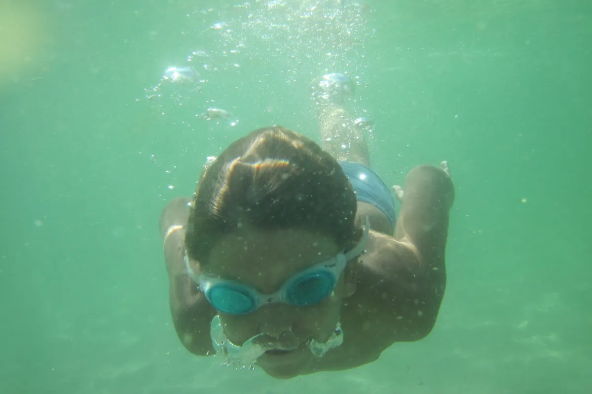 Child swimming underwater with goggles in clear shallow water