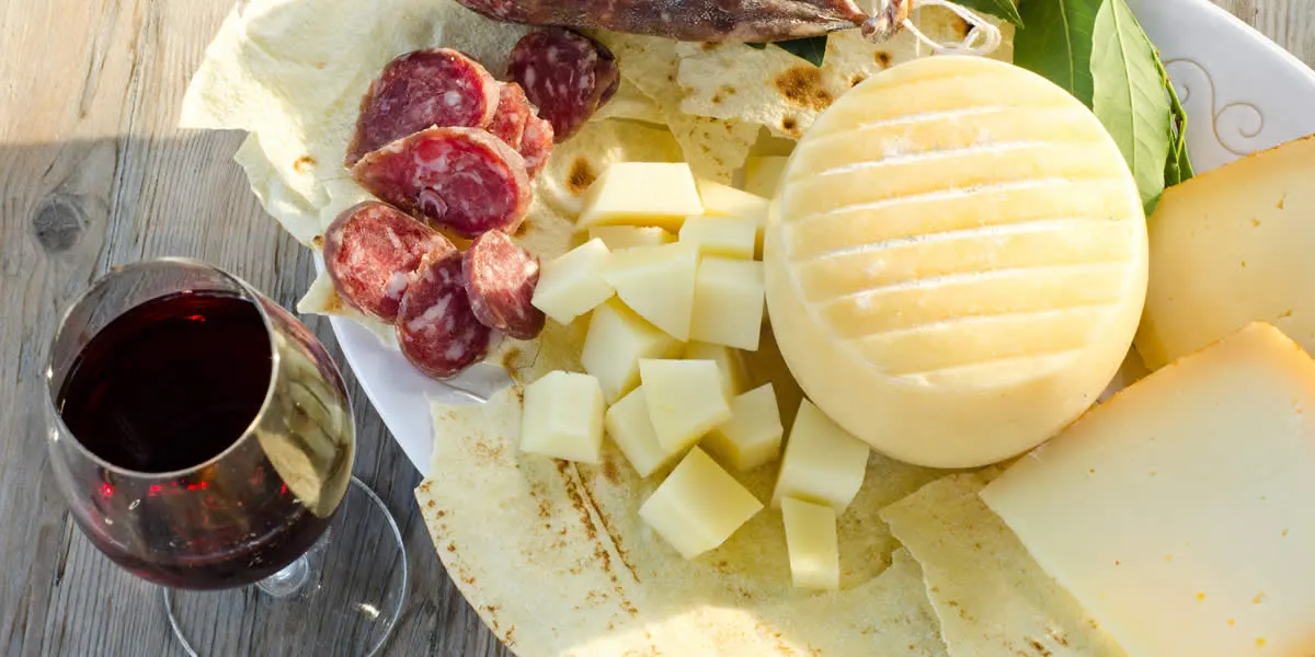 Sardinian pecorino, dried sausage, pane carasau and a glass of red wine on a wooden table