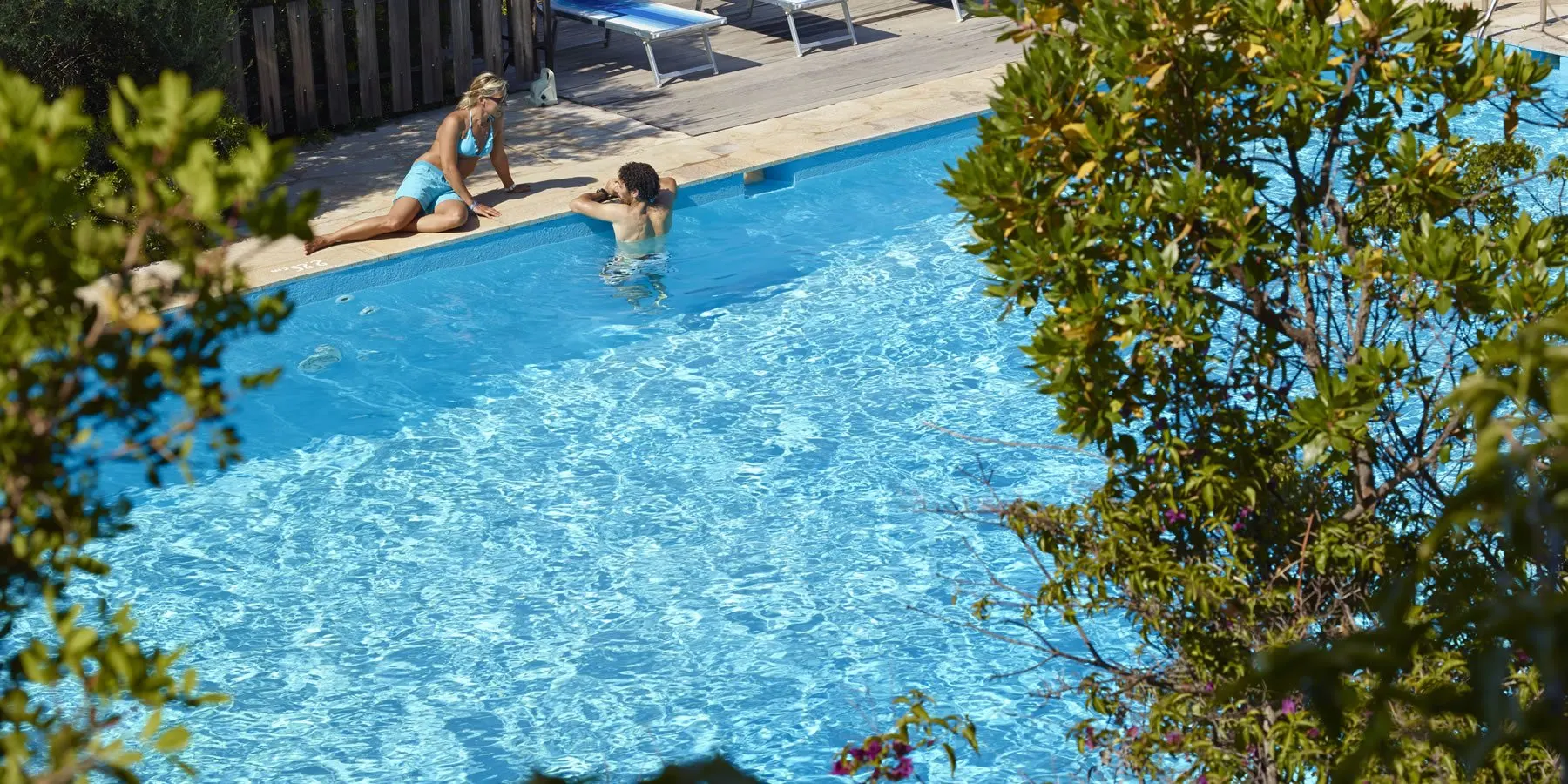 A mother and child at the edge of the garden pool, framed by green branches