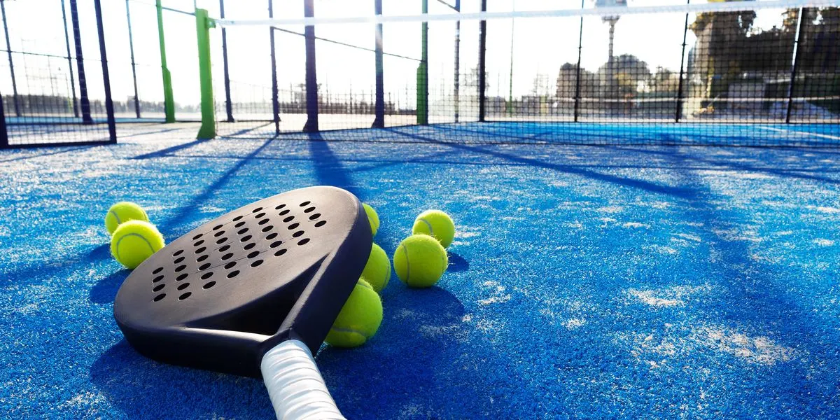 A padel racket and balls lying on the blue turf of the court