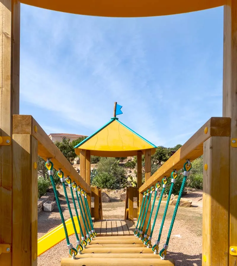 Wooden play tower with rope bridge in the village playground, granite rocks and junipers behind