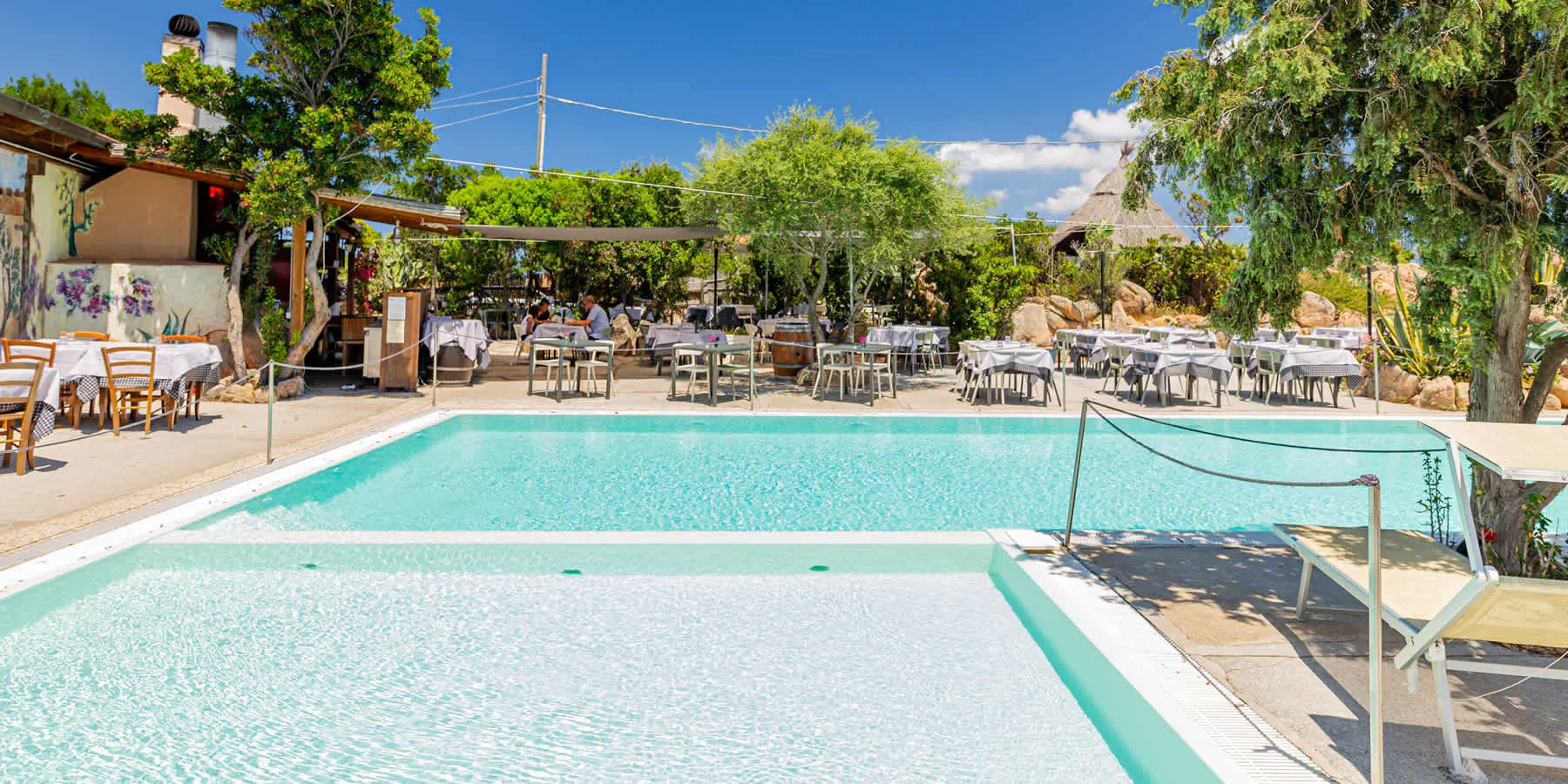 The two swimming pools of the village with the restaurant terrace and junipers behind