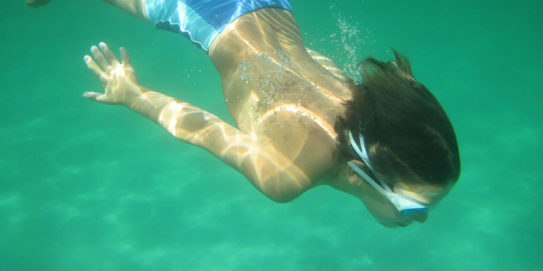 Child diving underwater with goggles in clear green sea water