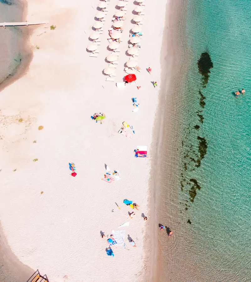 Aerial view of Porto Taverna beach in September, umbrellas in rows beside turquoise water