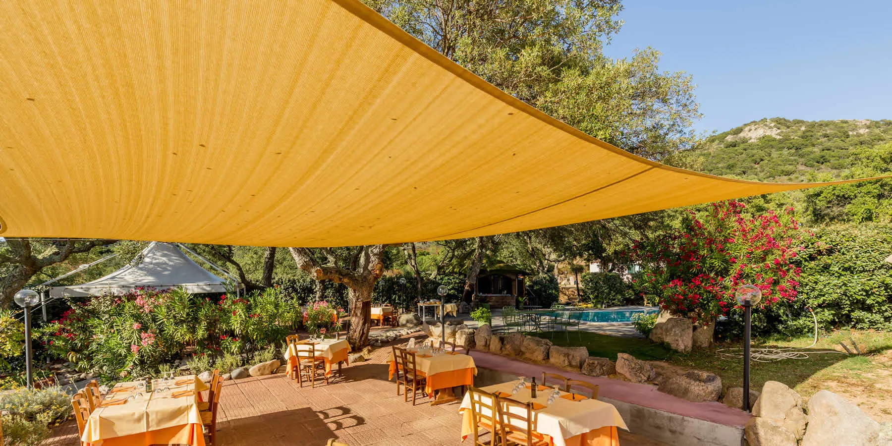 Country terrace of Borgo di Campagna with set tables under a large ochre shade sail, oleander and wooded hills around