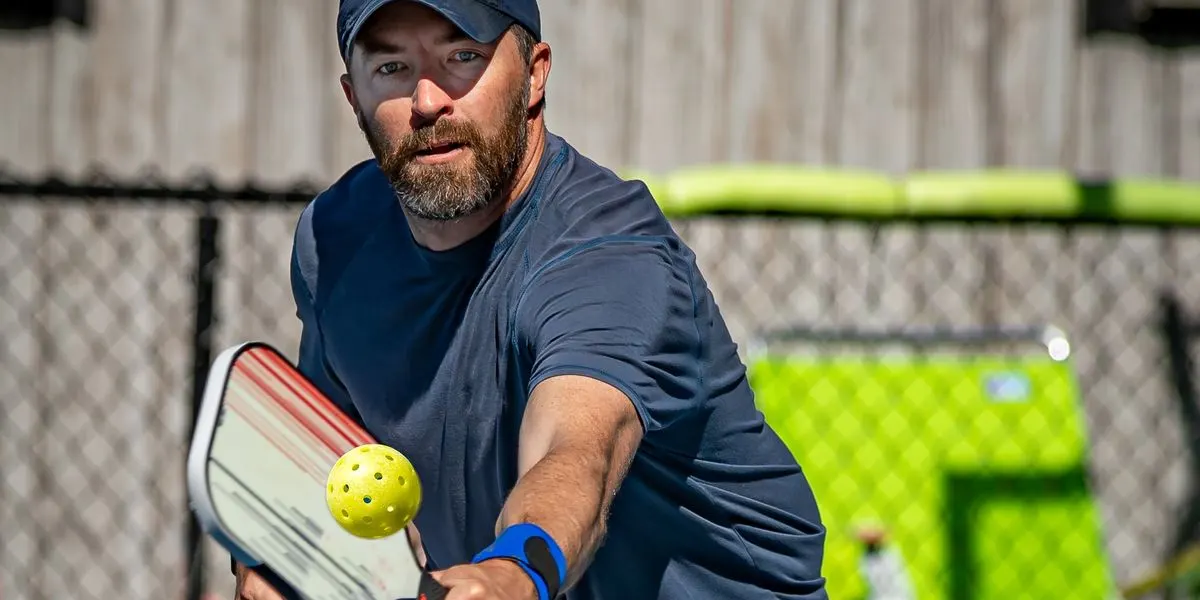 Focused pickleball player meeting the ball with a red and white paddle at the net