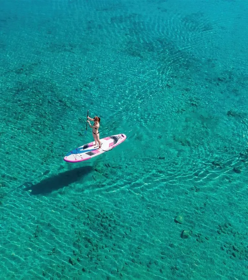 Aerial view of a lone paddleboarder casting a shadow on transparent turquoise water