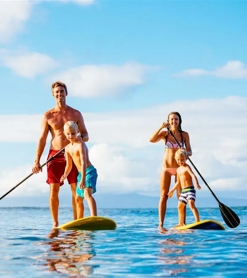 Parents and two children paddling side by side on stand-up paddleboards in calm water