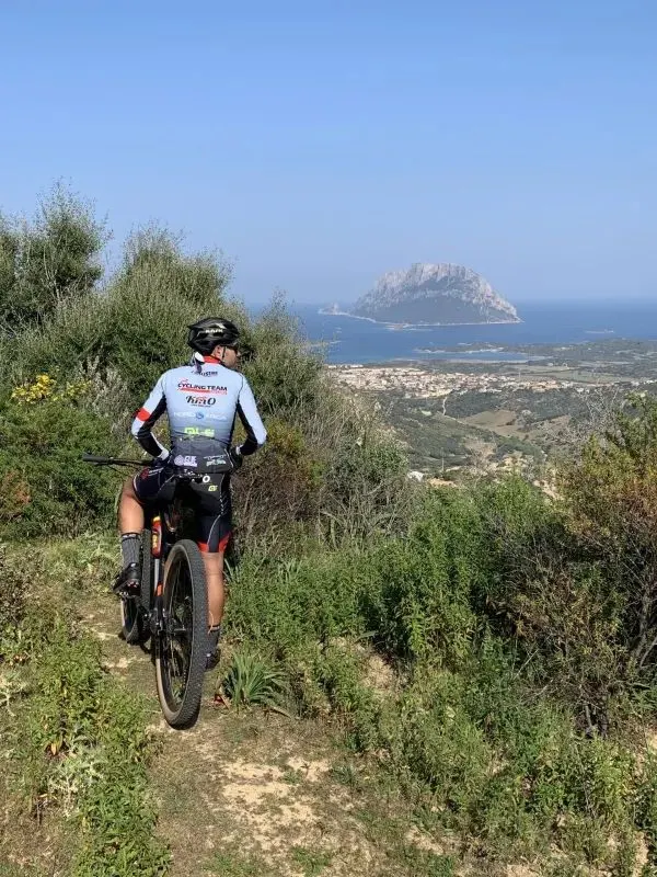Cyclist pausing on a high trail above the coast, Tavolara island rising from the sea in the distance