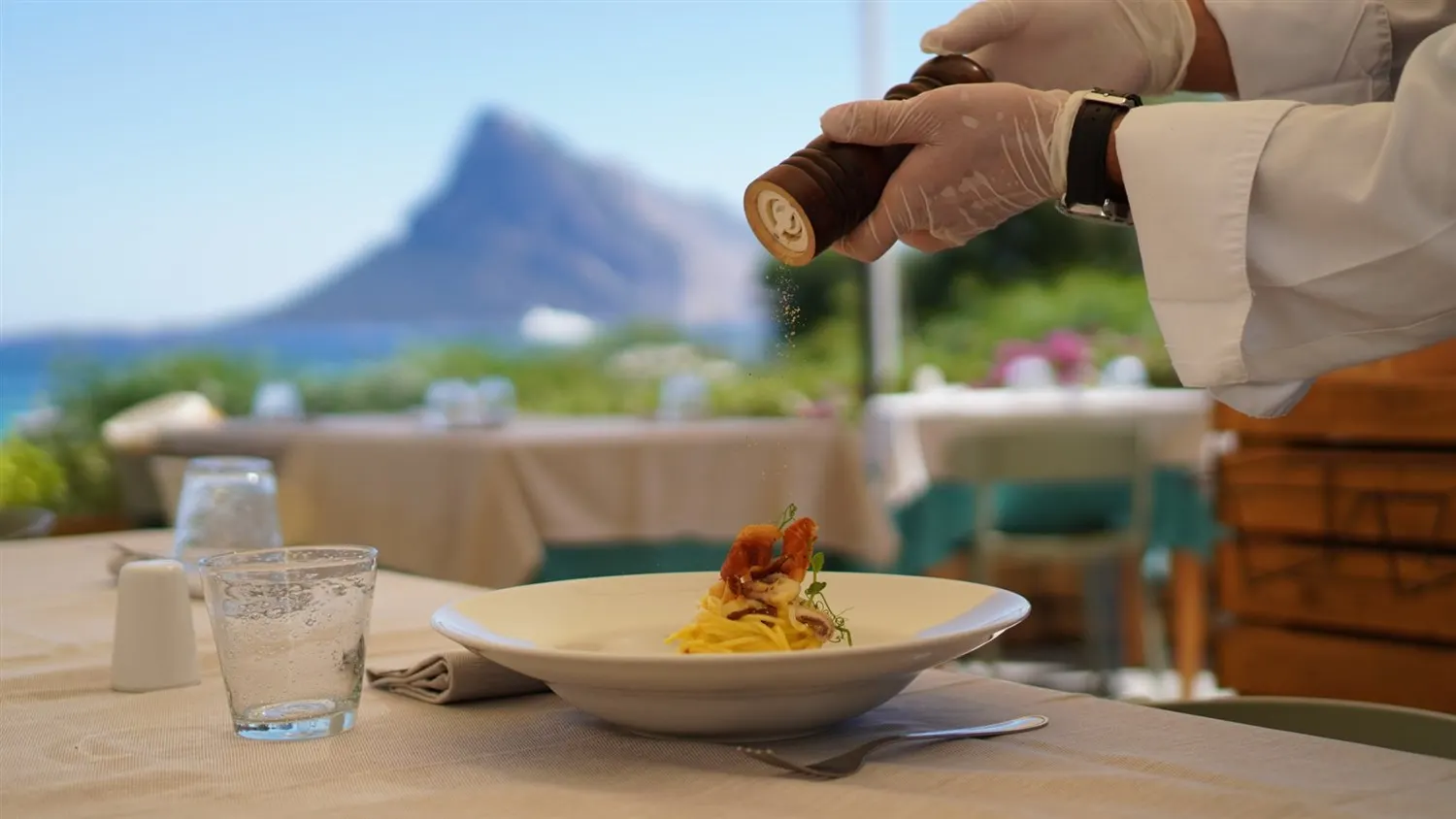Plate of fresh pasta being seasoned at a seafront table of La Tavernetta, Tavolara island in the background