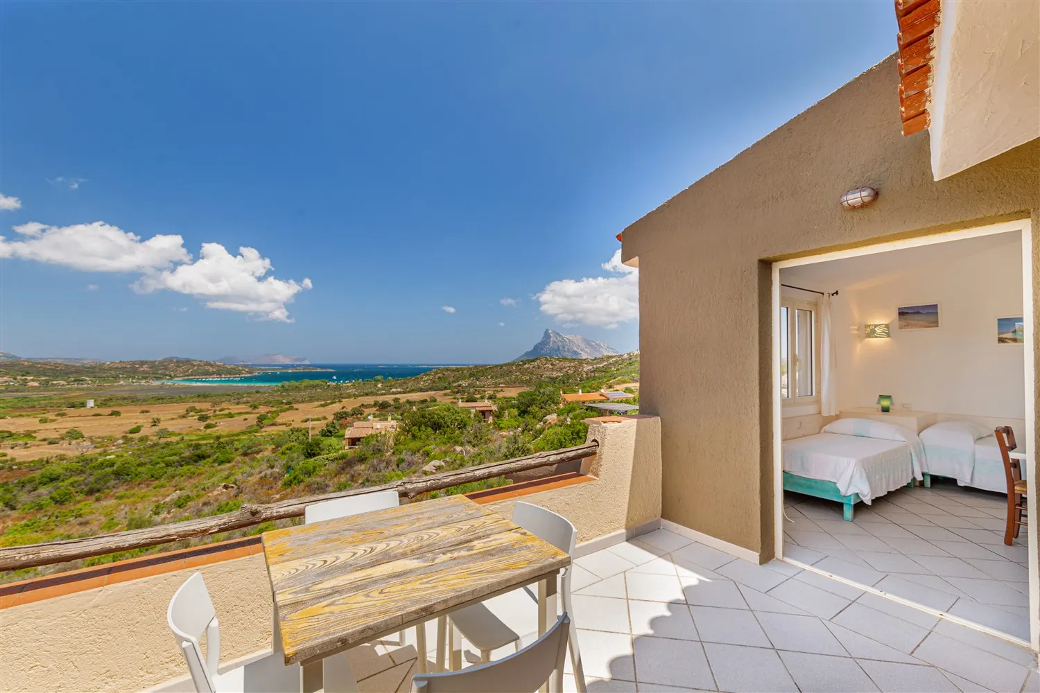 Apartment terrace with table, twin beds inside and the bay of Porto Taverna beyond